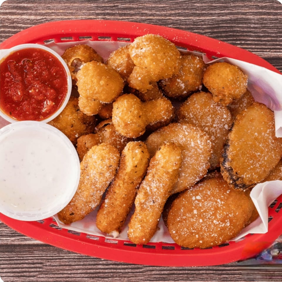A red basket filled with golden-brown fried appetizers, including mozzarella sticks and mushrooms, with two dipping sauces.