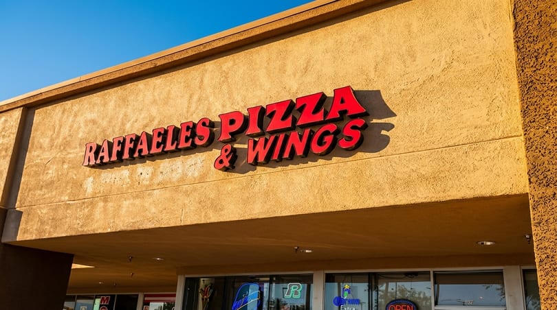 Raffaele's Pizza & Wings sign with red letters on a textured tan building under a blue sky.