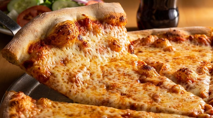 A slice of cheesy pizza being lifted from a whole pizza, with a side salad and drink.