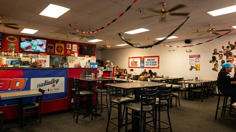 Interior of a casual restaurant with high-top tables, ceiling fans, and patrons dining.